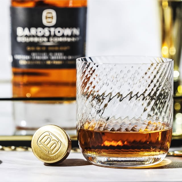 Close-up of Bardstown Bourbon poured in a textured glass with a gold bottle cap in front.