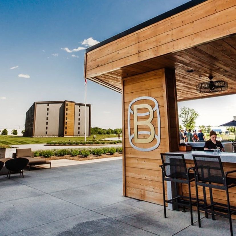 Outdoor bar area at Bardstown Bourbon Company with modern wooden design and distillery buildings in the background.